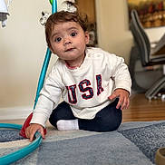 Maia Nicole joined the competition — help win amazing prizes! child, toddler, baby, sitting, portrait, smiling, wide_eyed, hair_bows, curly_hair, white_sweater, usa_sweater, dark_pants, sock, indoor, living_room, rug, toy, hoop, furniture, wood_floor