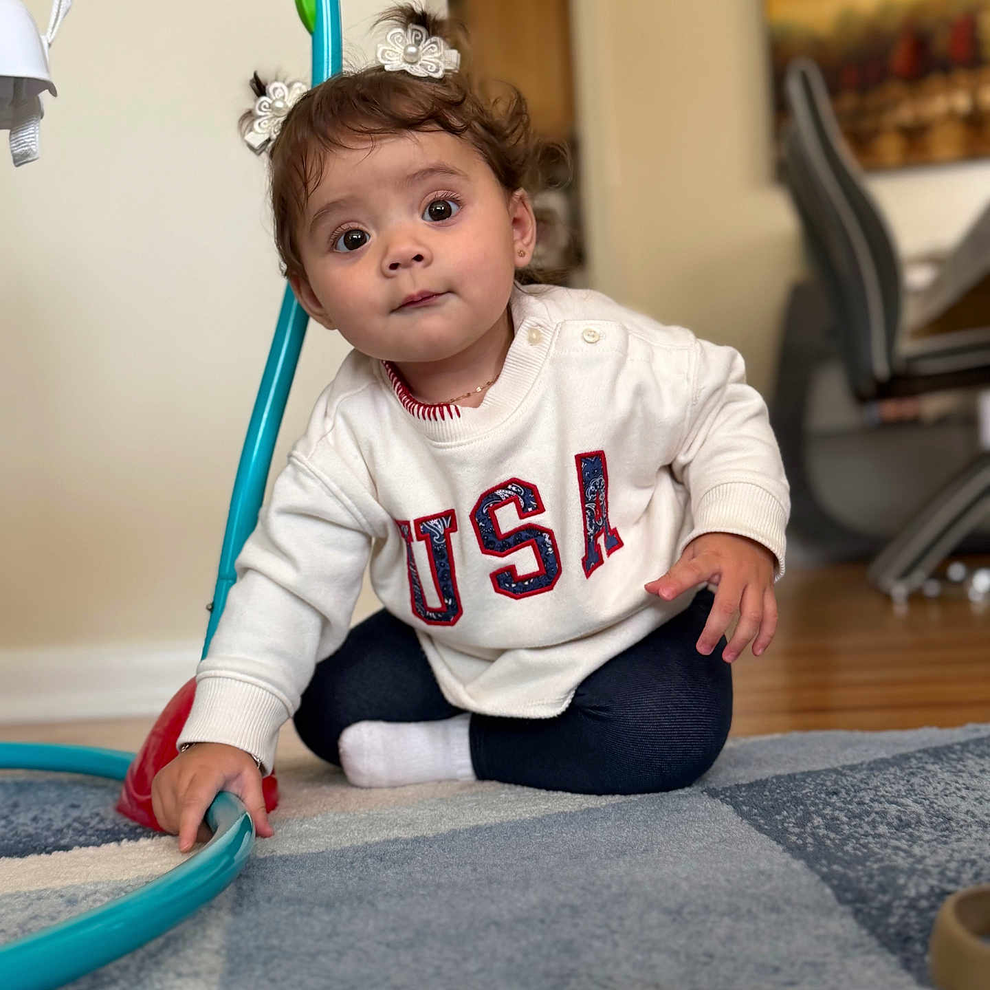 Maia Nicole joined the competition — help win amazing prizes! child, toddler, baby, sitting, portrait, smiling, wide_eyed, hair_bows, curly_hair, white_sweater, usa_sweater, dark_pants, sock, indoor, living_room, rug, toy, hoop, furniture, wood_floor