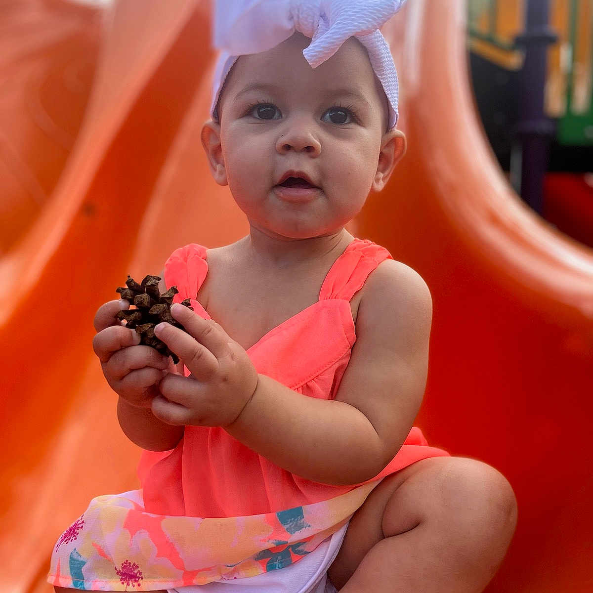 Estella is registered to the contest to win money with this photo: baby, bodypart, cap, clothing, dress, face, finger, food, hand, hat, head, outdoorplayarea, outdoors, person, photography, playarea, portrait, sitting, slide, toy