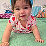 baby, child, crawling, headband, blue_bow, strawberry_pattern, pink_clothing, green_surface, pillow, colorful_background, indoors, cute, smiling, face, person, infant, young_child, happy, portrait, soft_lighting