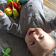 Bowen joined the competition — help win amazing prizes! baby, smiling, lying_down, grey_outfit, seal_design, plush_toy, colorful_toys, pacifier, blanket, indoor, wooden_floor, rug, cute, child, happy, infant, playful, soft_texture, portrait, young