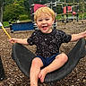 child, toddler, smiling, happy, playground, swing, outdoor, park, blond_hair, barefoot, cosmic_shirt, black_shirt, shorts, sitting, laughing, play_equipment, rope_climbing, wood_chips, trees, portrait
