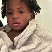 Kyrie is registered to the contest to win money with this photo: child, towel, curly_hair, indoors, portrait, close_up, young_child, face, skin, expression, soft_texture, bath_time, cozy, blanket, person, head, natural_light, brown_skin, relaxed, wrapped