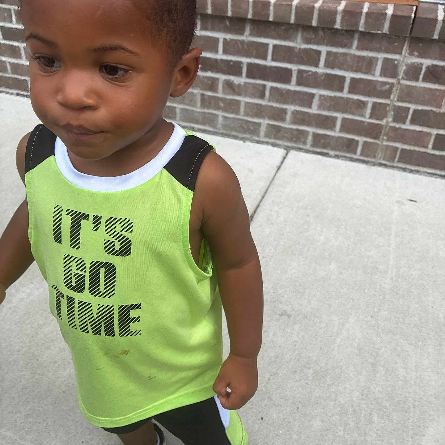 Kyrie joined the competition — help win amazing prizes! child, boy, tank_top, green_clothing, sneakers, sidewalk, brick_wall, outdoor, curious, standing, casual_wear, short_hair, young, person, daylight, urban, fashion, expression, concrete, footwear