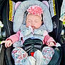 baby, sleeping, car_seat, headband, flower, elephant, soft_toy, pink, clothing, infant, child, safety_harness, cute, adorable, peaceful, floral_pattern, white_socks, pink_sleeves, seat_belt, outdoor