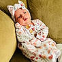 baby, infant, child, onesie, headband, floral_pattern, couch, sofa, fabric, buttons, soft_toys, comfort, relaxing, indoors, portrait, cute, peaceful, clothing, person, young