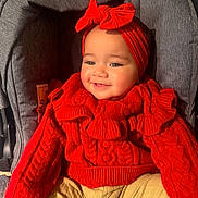 Prabhleen joined the competition — help win amazing prizes! baby, bow, child, cozy, cute, gray, happy, headband, indoors, infant, knitted_clothing, person, portrait, red_sweater, seated, smile, stroller, warm_lighting, yellow_pants, young_child