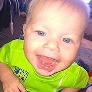 Lyall joined the competition — help win amazing prizes! baby, infant, child, smiling, open_mouth, blue_eyes, blond_hair, green_shirt, close_up, hands, tongue, teeth, drool, indoor, couch, blanket, window_light, playful, portrait, overexposed