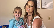 Adalynn is registered to the contest to win money with this photo: child, girl, adult, woman, smiling, portrait, family, indoor, kitchen, table, snack_bag, wall_sign, calendar, tattoo, dress, blue_shirt, brown_hair, seated, happy, photograph