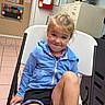 Adalynn joined the competition — help win amazing prizes! child, girl, toddler, smiling, portrait, indoors, chair, seated, blue_jacket, black_shorts, blonde_hair, office, filing_cabinet, door, bulletin_board, staff_shoutout, tile_floor, casual_clothing, happy, photograph