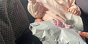 Havana is registered to the contest to win money with this photo: baby, child, pink_sweater, package, couch, blanket, indoors, cozy, person, hand, leg, footwear, sock, light, window, furniture, relaxation, curly_hair, cute, expression