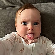 Scout joined the competition — help win amazing prizes! baby, infant, child, tongue_out, sticking_tongue, onesie, pajamas, rainbow_pattern, close_up, portrait, blue_eyes, long_eyelashes, couch, sofa, indoor, cute, expression, hand, cheeks, cozy