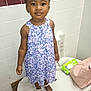 child, girl, dress, floral_pattern, shoes, sparkly, hair_accessory, bathroom, tiles, changing_table, bag, baby_wipes, standing, portrait, cute, smiling, person, indoor, fashion, accessories