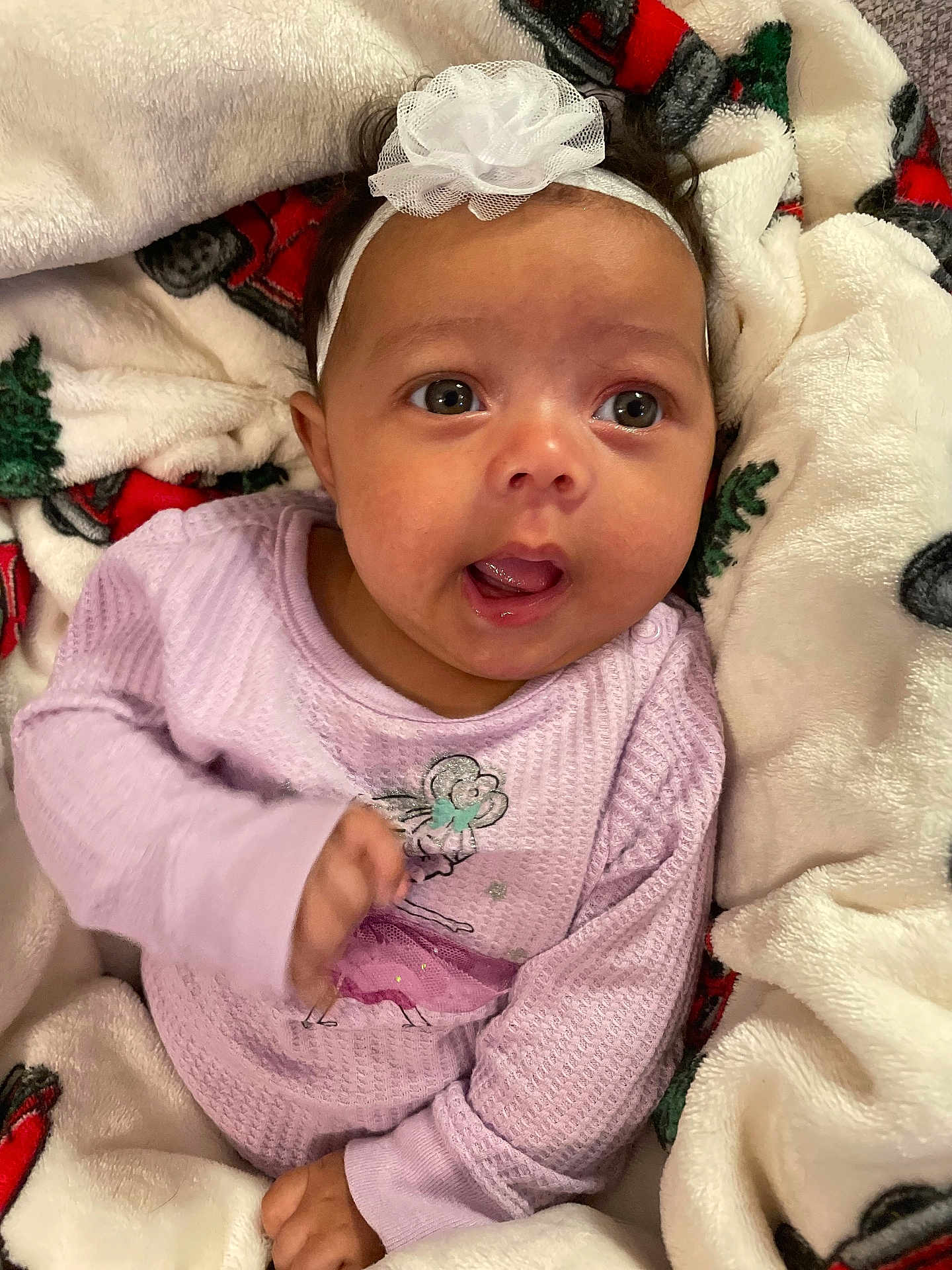 Maddie joined the competition — help win amazing prizes! baby, infant, headband, flower, purple_clothing, blanket, holiday_pattern, cozy, cute, indoors, child, person, smile, expression, portrait, young_child, soft_texture, warm, candid, happy