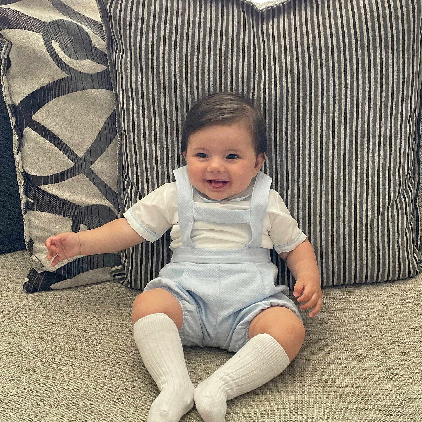Lucus is registered to the contest to win money with this photo: baby, child, clothing, couch, cute, face, furniture, happy, head, home, indoor, infant, person, pillow, portrait, romper, sitting, smiling, white_socks, young