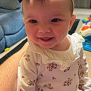 Amirah is registered to the contest to win money with this photo: baby, child, infant, smiling, portrait, bow, headband, floral_clothing, long_sleeves, pants, sitting, indoor, living_room, home, couch, toy, adult_arm, face, happy, photography