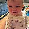 baby, child, infant, smiling, portrait, bow, headband, floral_clothing, long_sleeves, pants, sitting, indoor, living_room, home, couch, toy, adult_arm, face, happy, photography