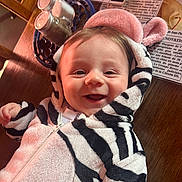 Romain a rejoint le concours — aidez-le/la à gagner de superbes lots ! baby, child, smiling, zebra_onesie, hood, ears, table, wood, salt_shaker, pepper_shaker, newspaper, happy, cute, cozy, indoor, person, face, infant, clothing, portrait