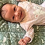 baby, infant, smile, face, hand, clothing, onesie, blanket, pattern, animal_print, happy, cute, lying_down, child, skin, head, small_fingers, indoor, young, person