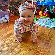 Annabel is registered to the contest to win money with this photo: animal_prints, baby, child, clothing, colorful, crawling, cute, floor, happy, head, headband, indoors, infant, pastel_colors, person, playroom, smiling, storage_bins, toys, wooden_floor