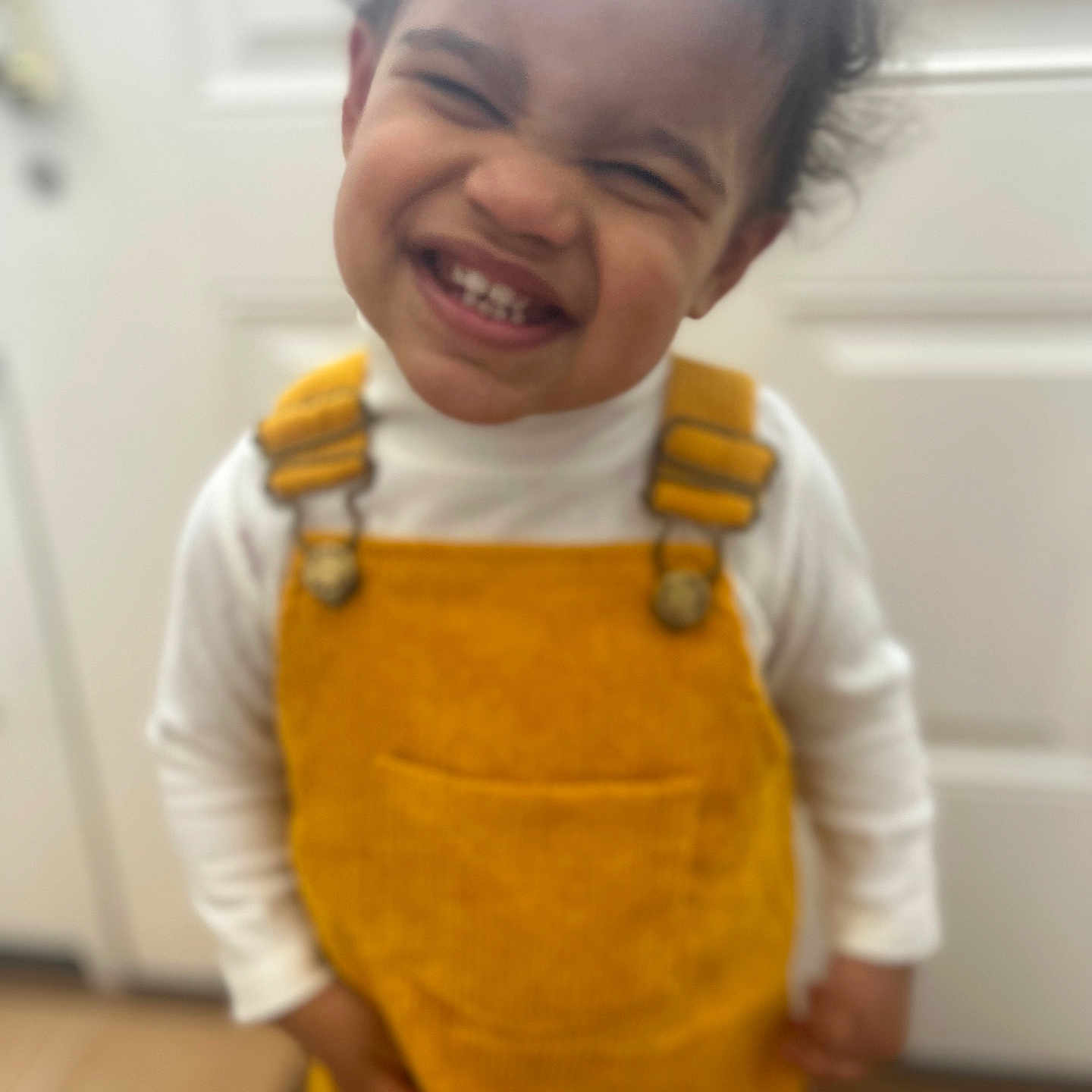 Cienna joined the competition — help win amazing prizes! child, clothing, curly_hair, cute, door, expression, face, fun, hair, happy, indoor, joy, person, portrait, smiling, standing, toddler, white_shirt, yellow_overall, young_child