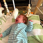 Bowen joined the competition — help win amazing prizes! baby, infant, smiling, onesie, blanket, toy, wooden_toy, hanging_toy, indoor, floor, child, happy, face, person, wood, pattern, fabric, cute, playtime, cozy