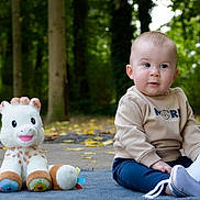 Manoe a rejoint le concours — aidez-le/la à gagner de superbes lots ! baby, child, plush_toy, giraffe, outdoor, forest, blanket, autumn_leaves, sitting, curious, casual_clothing, footwear, nature, young_child, toy, greenery, daylight, cute, person, portrait