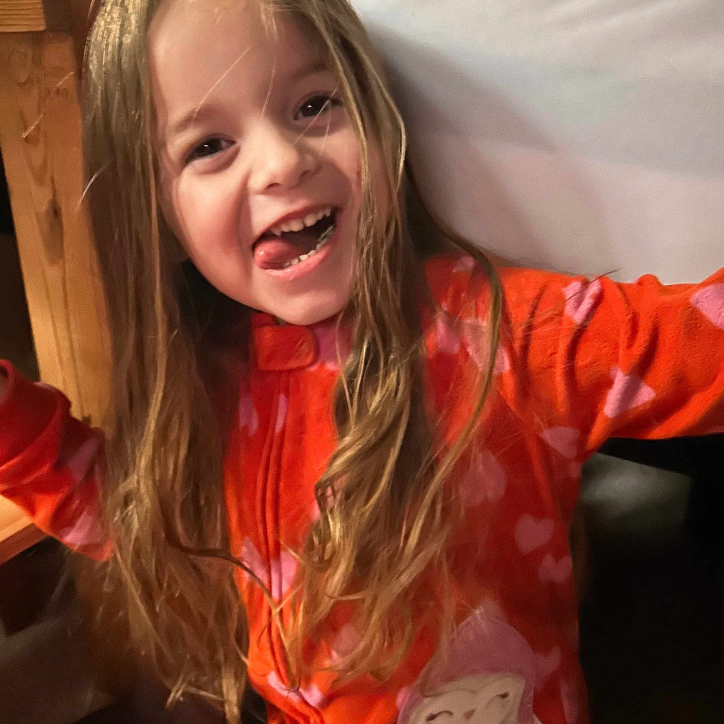 Aspyn joined the competition — help win amazing prizes! child, cozy, cute, face, fun, girl, happy, hearts_pattern, indoor, long_hair, orange_clothing, pajamas, person, playful, portrait, smiling, tongue_out, warm_lighting, wooden_furniture, young