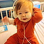 baby, child, hospital, bed, medical, nasal_tubes, headphones, orange_outfit, smiling, happy, indoor, furniture, person, healthcare, cute, infant, medical_tape, hospital_room, baby_girl, sitting