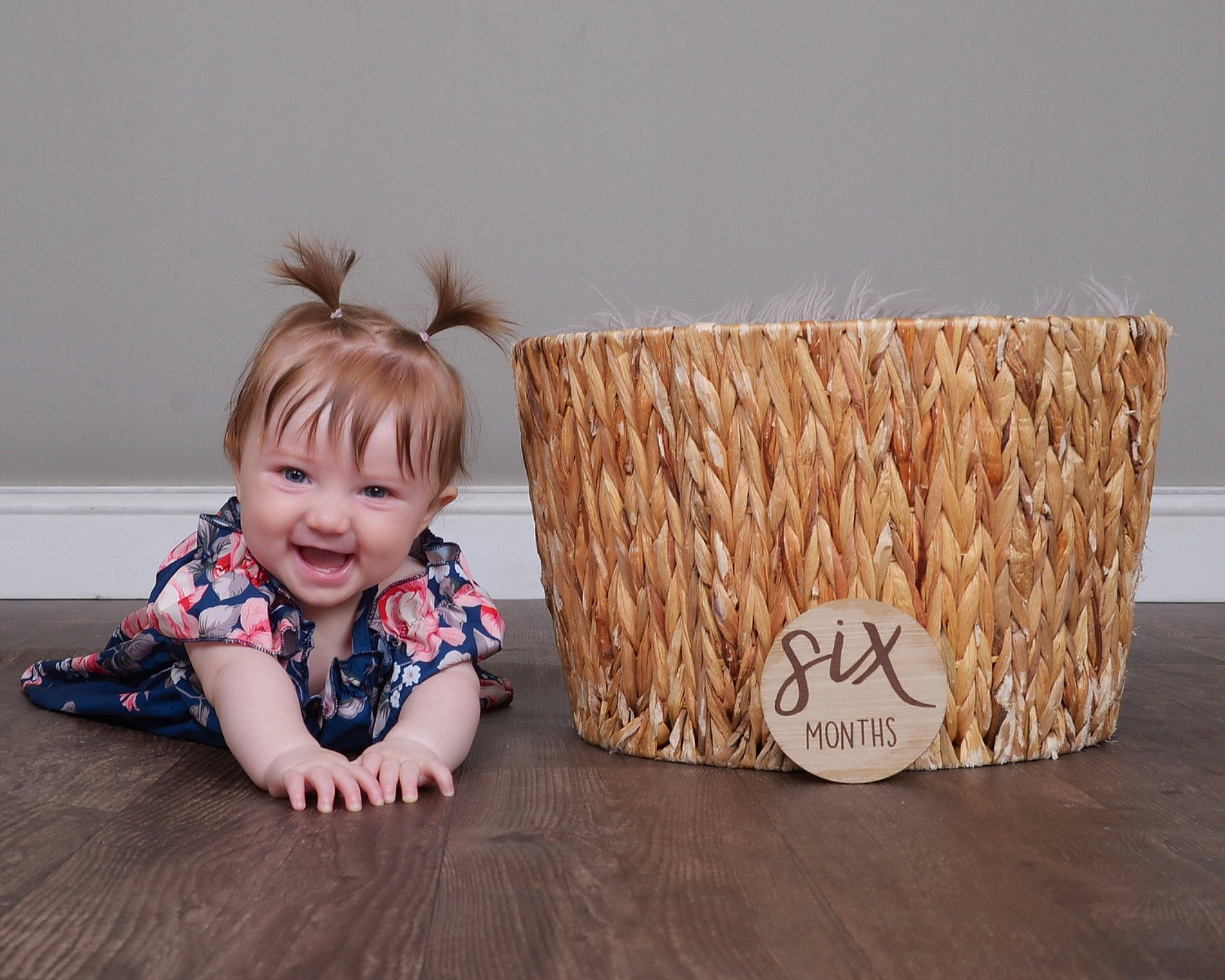Olivia is registered to the contest to win money with this photo: baby, baby_toddler_clothing, basket, child, event, flooring, grass, happy, hardwood, joy, pattern, person, picnic_basket, room, sitting, smile, storage_basket, toddler, wicker, wood