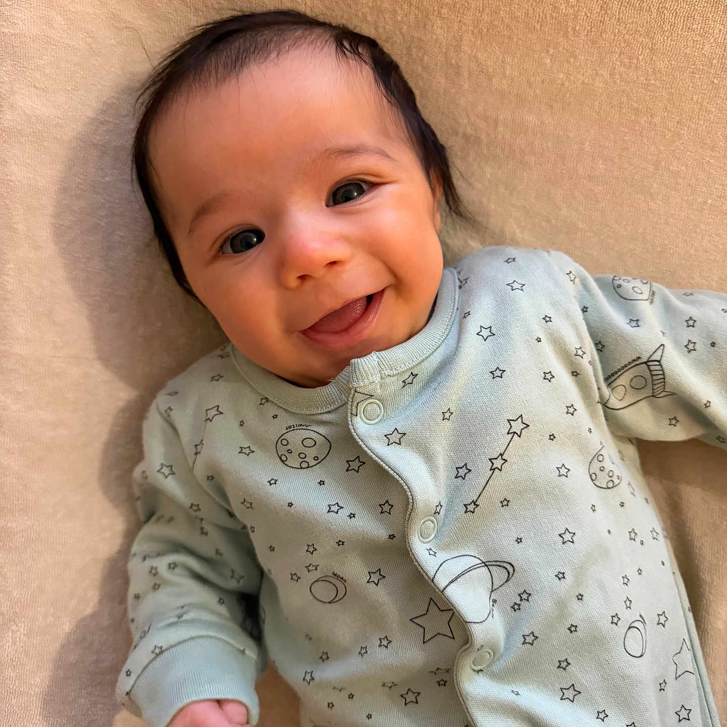 Youssef a rejoint le concours — aidez-le/la à gagner de superbes lots ! baby, beige_background, child, clothing, cozy, cute, face, happy, infant, lying_down, newborn, onesie, planets, portrait, rocket, smile, soft_texture, space_theme, stars, warm_lighting