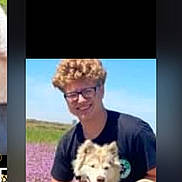 Harley joined the competition — help win amazing prizes! casual_clothing, crouching, curly_hair, daytime, dog, field, flowers, friendship, glasses, grass, happy, leash, man, nature, outdoor, pet, portrait, sky, smile, sunny