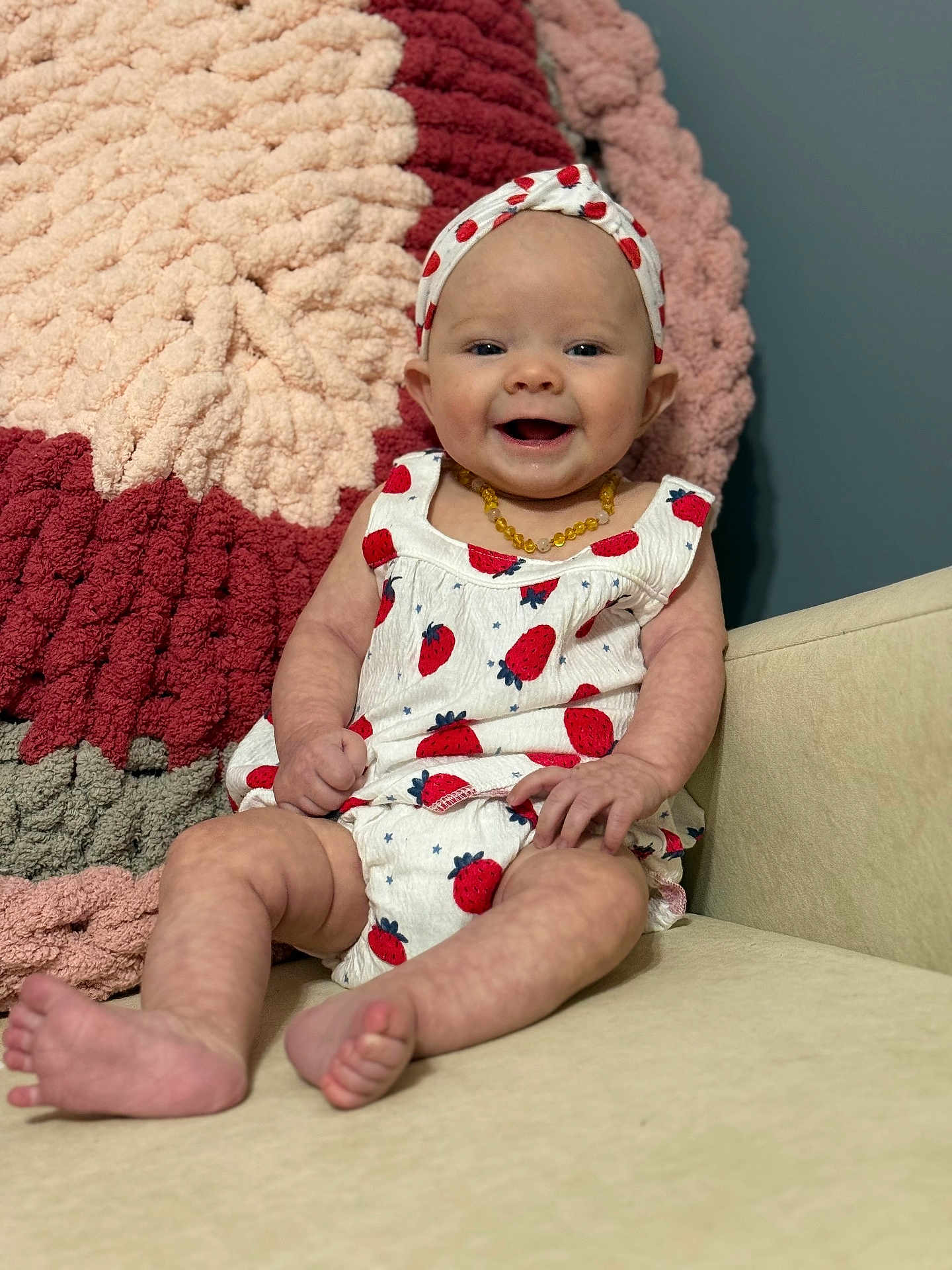 Emma Kaye is registered to the contest to win money with this photo: baby, infant, smiling, sitting, headband, strawberry_pattern, clothing, blanket, couch, happy, cute, indoor, portrait, child, furniture, skin, feet, hand, face, yellow_necklace