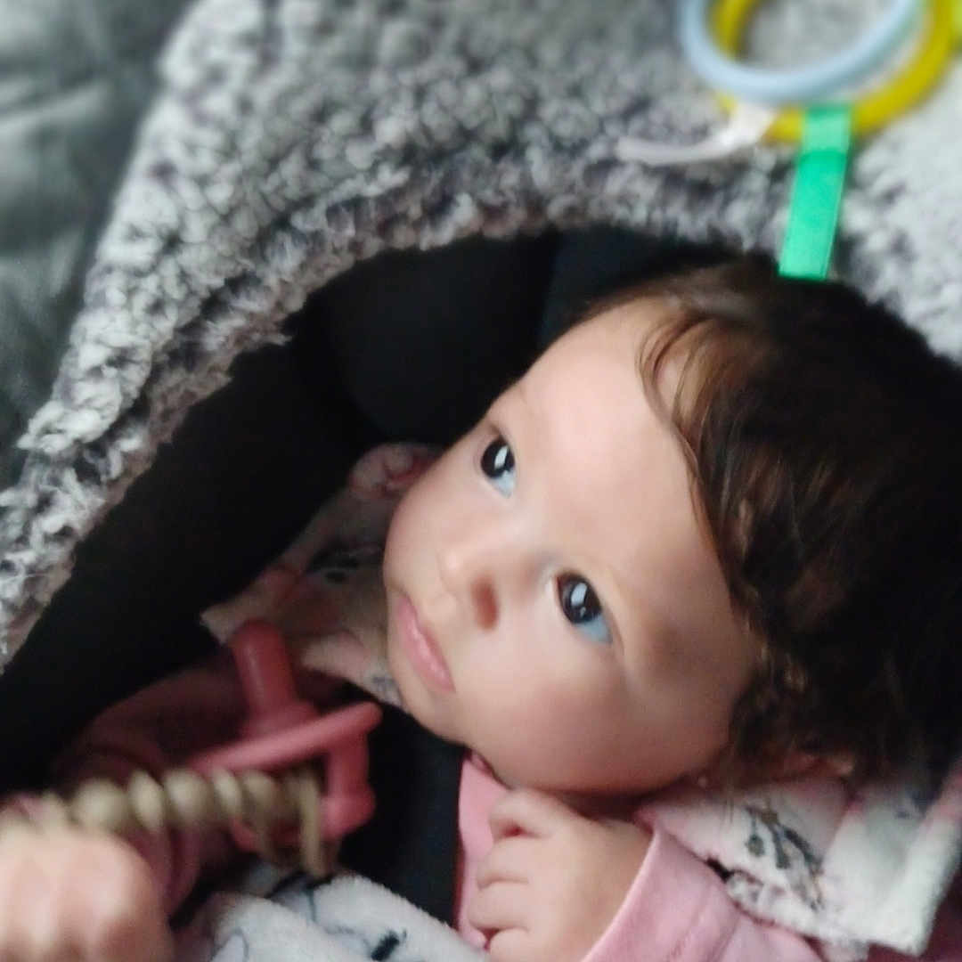 Zaylee joined the competition — help win amazing prizes! baby, child, blanket, toy, indoor, infant, cute, cozy, soft_texture, pink_clothing, curious_look, face, portrait, young_child, warm, comfort, seated, hand, head, expression