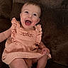 baby, child, smiling, happy, sitting, dress, peach, cute, infant, portrait, indoors, person, couch, furniture, skin, face, legs, hand, ruffles, joyful