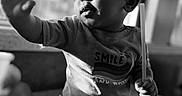 Da'Vonnie joined the competition — help win amazing prizes! baby, child, infant, crown, paper_crown, sitting, smiling, curious, reaching, hand, stick, shirt, text_on_clothing, black_and_white, portrait, indoor, window_light, dramatic_lighting, floor, birthday