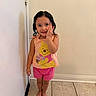 child, toddler, barefoot, standing, smiling, winnie_the_pooh, tank_top, pink_shorts, indoor, tile_floor, wall, door, curly_hair, cute, happy, person, portrait, casual_clothing, young, small