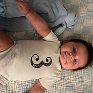 Sebastian joined the competition — help win amazing prizes! baby, infant, onesie, mustache_design, blanket, stuffed_animal, blue, white_clothing, smiling, lying_down, cute, child, soft_toy, indoor, portrait, happy, toddler, face, hand, cozy