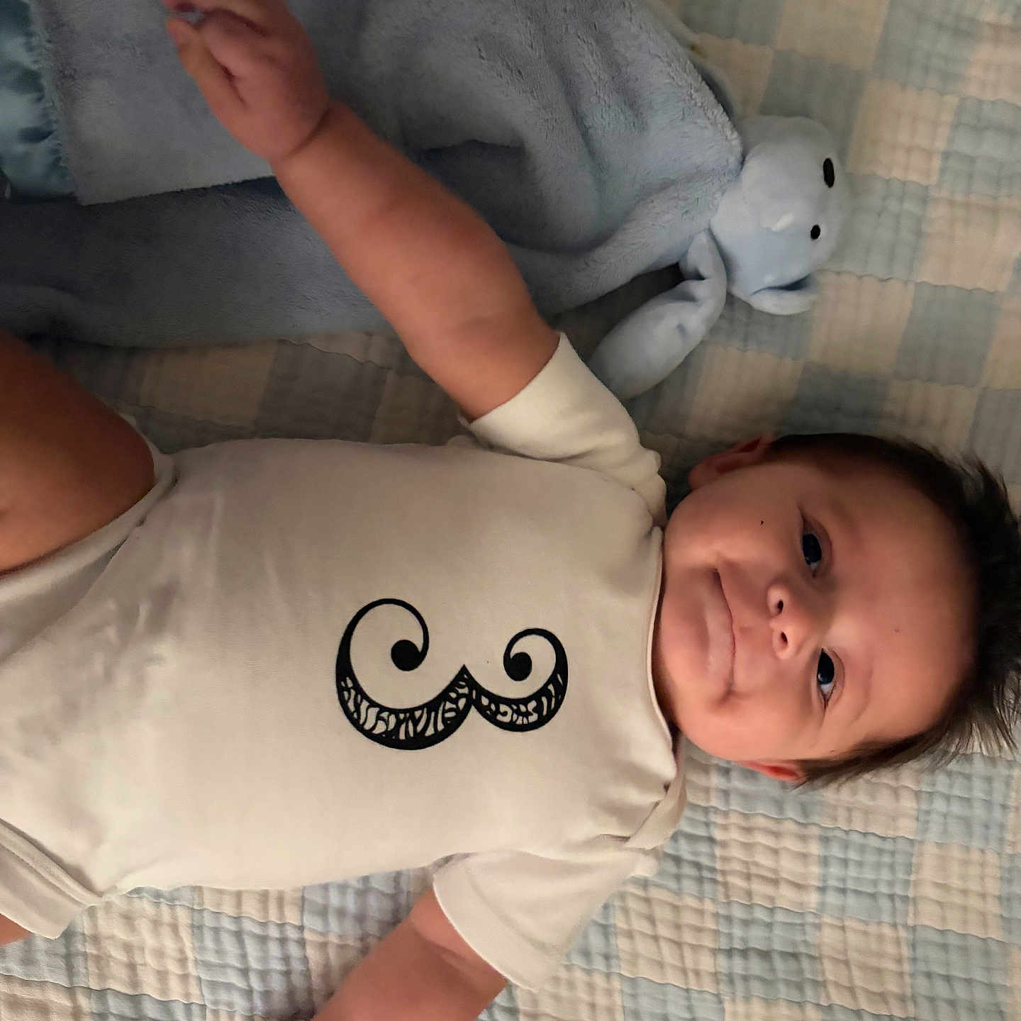 Sebastian joined the competition — help win amazing prizes! baby, infant, onesie, mustache_design, blanket, stuffed_animal, blue, white_clothing, smiling, lying_down, cute, child, soft_toy, indoor, portrait, happy, toddler, face, hand, cozy