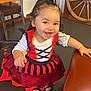 toddler, child, smiling, dress, costume, pirate, red, black, indoor, wooden_furniture, chair, floor, happy, girl, person, hair, table, shoes, face, playful