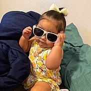 Serenity joined the competition — help win amazing prizes! baby, sunglasses, bow, floral_outfit, cushion, blue_blanket, teal_blanket, child, indoor, cute, fashion, portrait, person, sitting, playful, accessory, headwear, smile, skin, young
