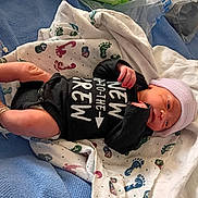 Tayshawn is registered to the contest to win money with this photo: newborn, baby, infant, hospital, blanket, footprints, onesie, hat, lying_down, medical_tube, hospital_id_band, bed, pink, black_clothing, white_blanket, blue_blanket, person, cute, sleepwear, newborn_clothes