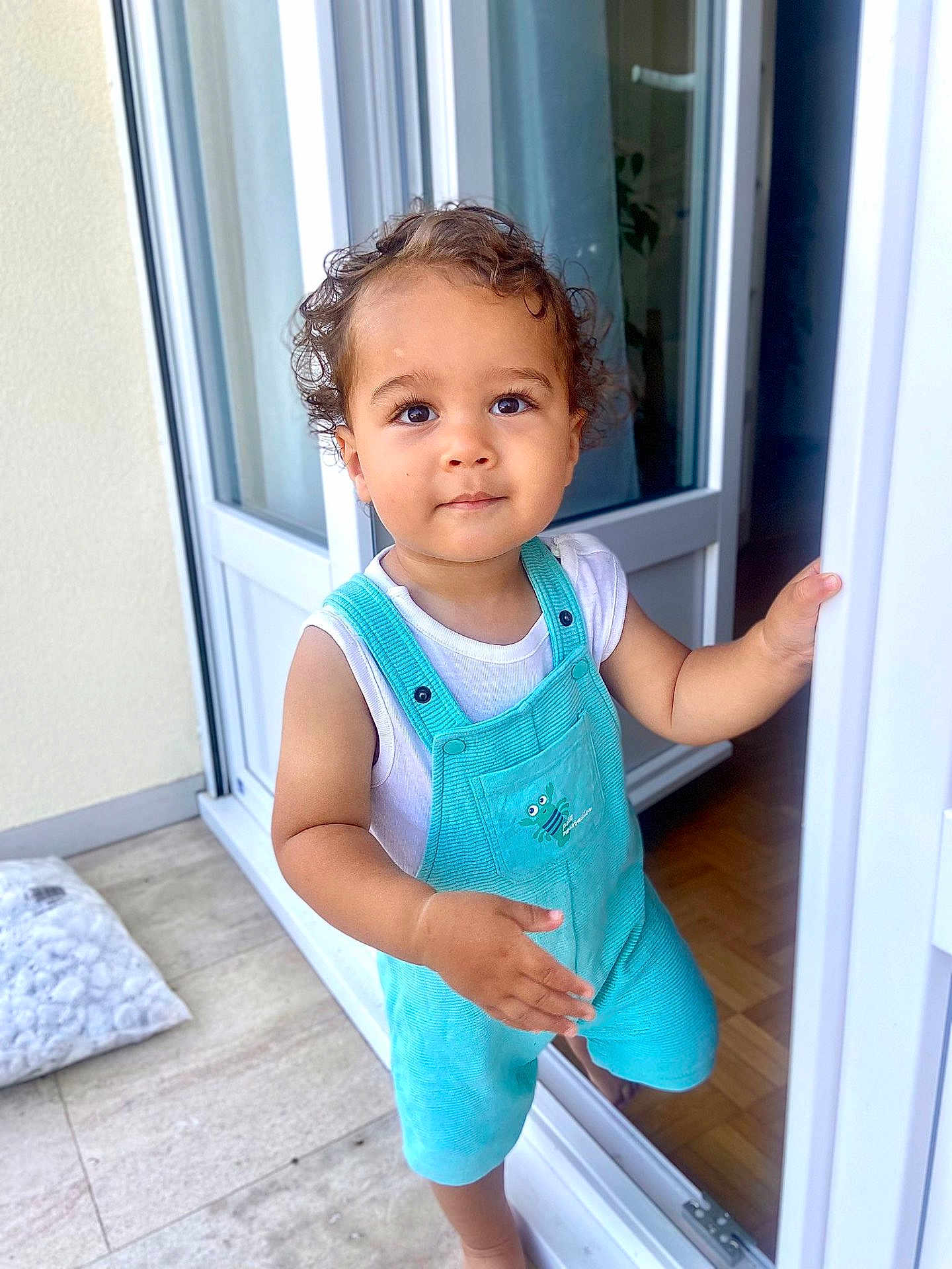 Andréa a rejoint le concours — aidez-le/la à gagner de superbes lots ! toddler, child, curly_hair, overalls, turquoise, white_shirt, doorway, indoors, outdoors, floor, window, curtain, hand, standing, looking_up, cute, portrait, baby, person, home