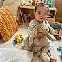 toddler, child, plush_toy, bunny, carpet, cushion, teddy_bear, books, toy_blocks, shelf, sock, yellow_towel, indoor, smiling, hair_tie, wooden_furniture, soft_toy, playroom, baby, floor