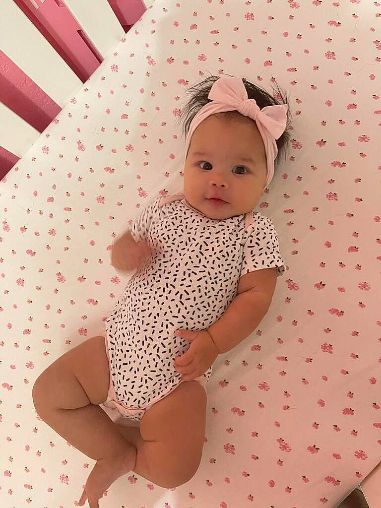 Aubriella is registered to the contest to win money with this photo: baby, baby_toddler_clothing, cap, child, clothing, comfort, human_leg, knee, linens, magenta, one_piece_garment, pattern, person, pink, room, skin, sleeve, textile, thigh, toddler