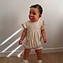 toddler, child, pacifier, romper, shoes, hair_clip, wooden_floor, white_wall, standing, indoor, natural_light, shadow, cute, baby, footwear, person, infant, one_child, looking_sideways, short_sleeves