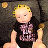 baby, black_clothing, bokeh, child, couch, cute, face, feet, filter, flower_crown, hand, head, indoor, infant, legs, onesie, portrait, sitting, sofa, sunflower
