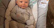 Navha is registered to the contest to win money with this photo: baby, infant, onesie, baby_seat, floor, wooden_floor, sock, cushion, clothing, face, person, indoor, cute, smile, newborn, resting, child, home, baby_boy, cozy