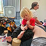 Robert is registered to the contest to win money with this photo: toddler, child, bed, marker, blond_hair, person, adult, glasses, curly_hair, blanket, toy, indoor, window, fan, curtain, sitting, casual_clothing, relaxed, family, room
