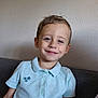 child, boy, smiling, polo_shirt, light_blue, sitting, couch, indoor, wall, short_hair, casual_clothing, portrait, happy, person, cute, young, comfortable, home, relaxed, face